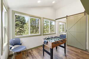 Living room/game/recreation room featuring LVP floors, a barn door to the bedroom, vaulted ceiling, and recessed lighting