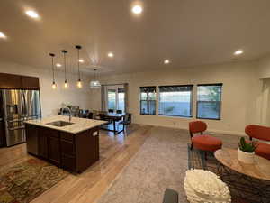Kitchen with stainless steel appliances, dark wood finish cabinetry, light stone counters, and an island with sink