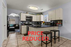 Kitchen featuring cream-colored cabinetry, stainless steel appliances, dark countertops, and a gray tile backsplash