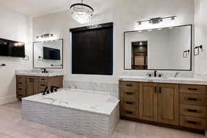 Bathroom with two vanities, light tile patterned floors, a garden tub, and a chandelier