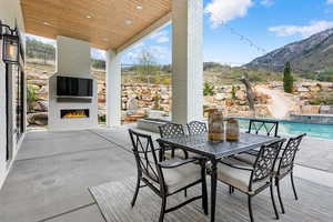 View of patio with a lit fireplace, outdoor dining space, and an outdoor pool