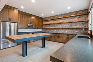 Kitchen with stainless steel appliances, open shelves, brick wall, recessed lighting, and finished concrete floors