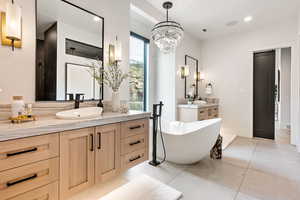 Full bath with two vanities, light tile patterned flooring, a freestanding bath, and suspended lighting