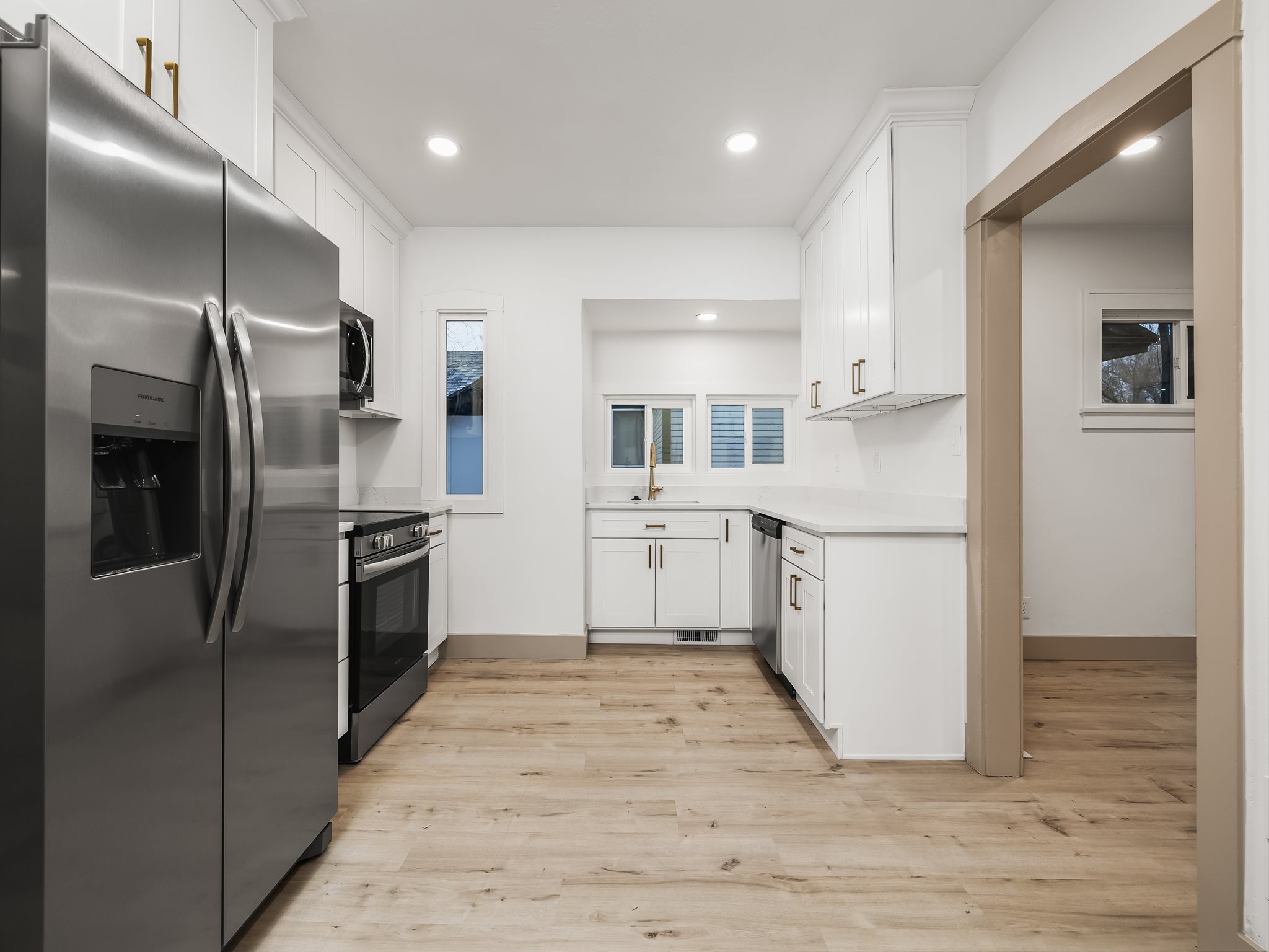 Kitchen featuring stainless steel appliances, white cabinets, light wood-type flooring, recessed lighting, and light stone countertops