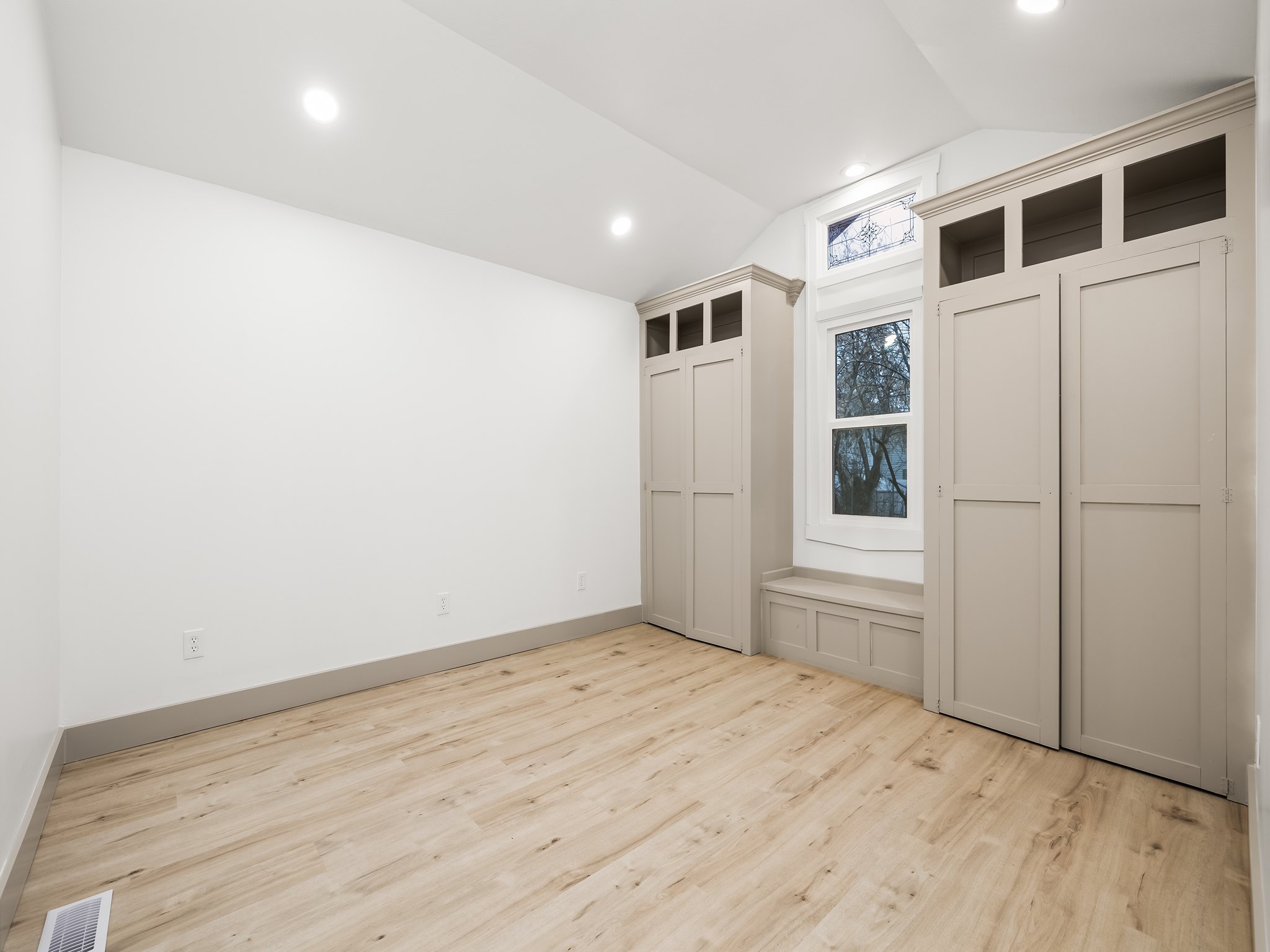 Unfurnished bedroom featuring two closets, vaulted ceiling, and light wood-style flooring