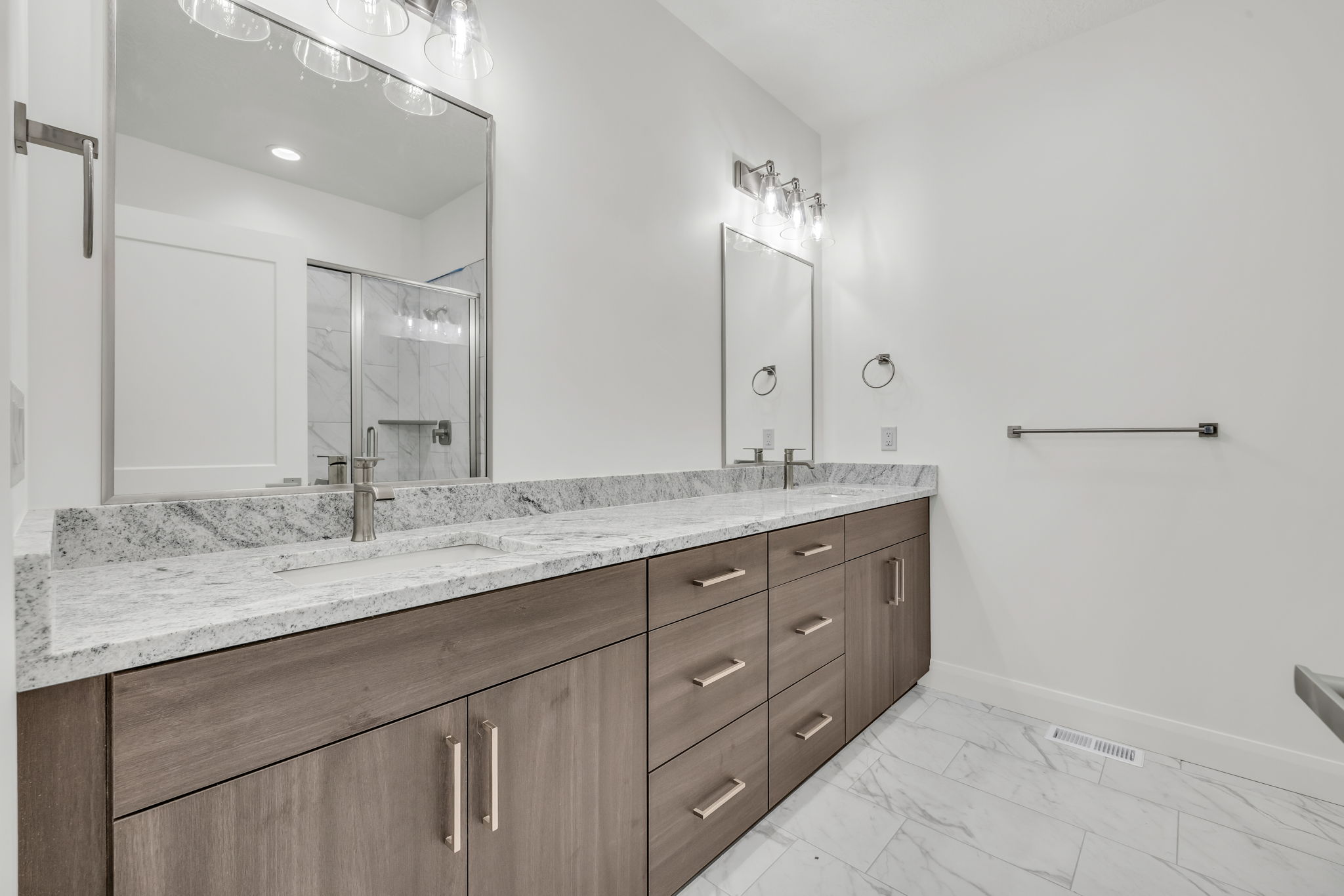 Bathroom featuring double vanity, a marble finish shower, and light marble finish floors