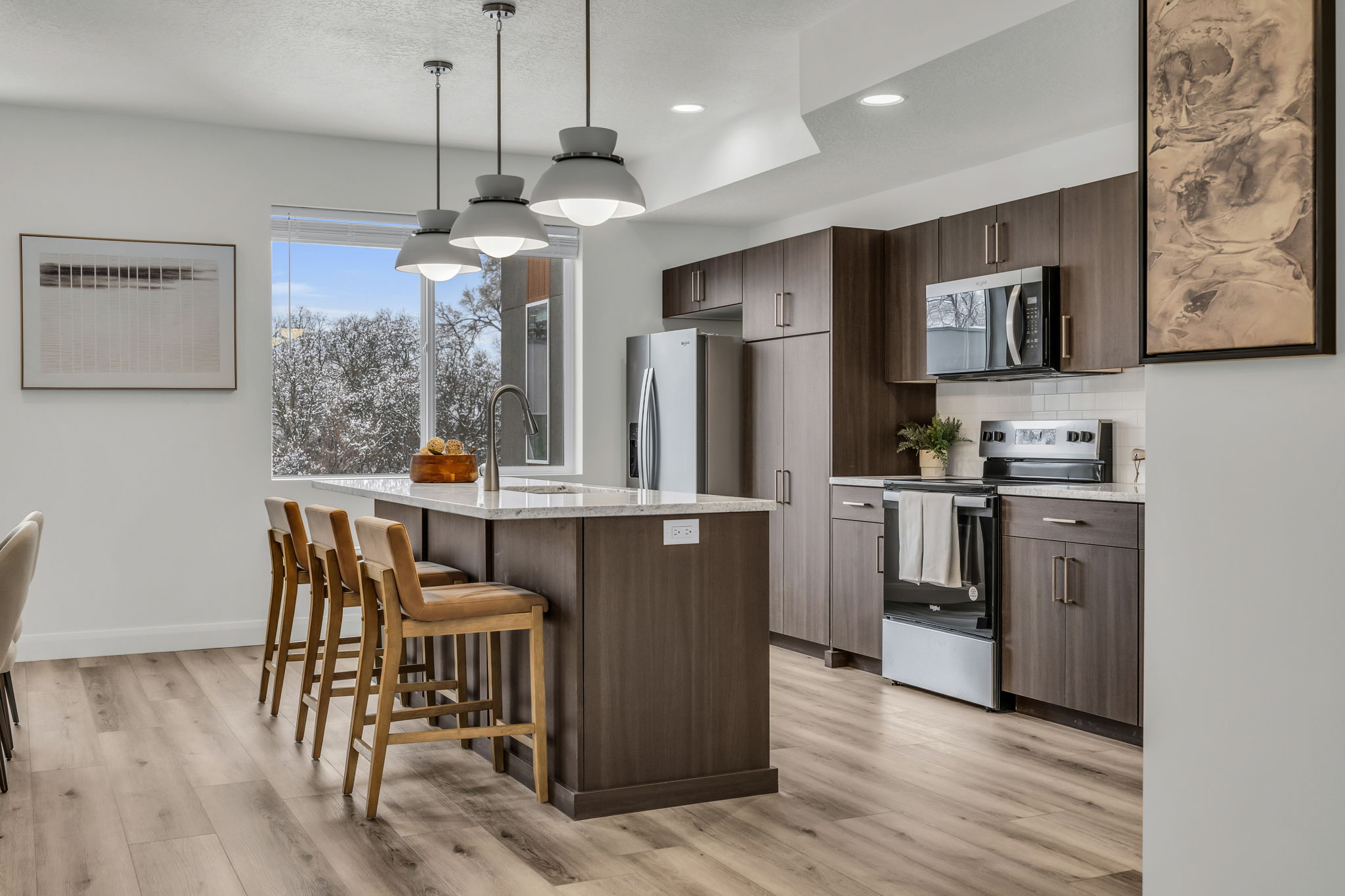 Kitchen featuring stainless steel appliances, dark wood finish cabinets, light wood-type flooring, a kitchen bar, and a kitchen island with sink