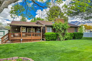 View of front of home with brick siding, a front yard, a wooden deck, a chimney, and roof with shingles