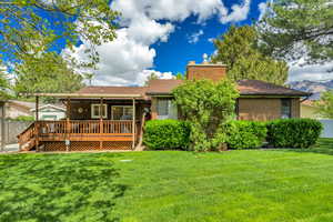 Rear view of property featuring a deck, brick siding, a chimney, and a shingled roof