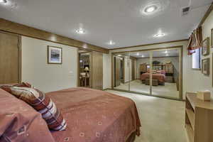 Bedroom with a closet, light colored carpet, and a textured ceiling