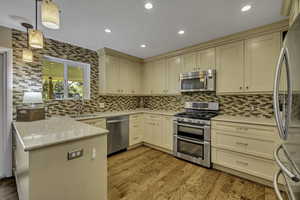 Kitchen featuring stainless steel appliances, a peninsula, decorative light fixtures, light stone countertops, and cream cabinets
