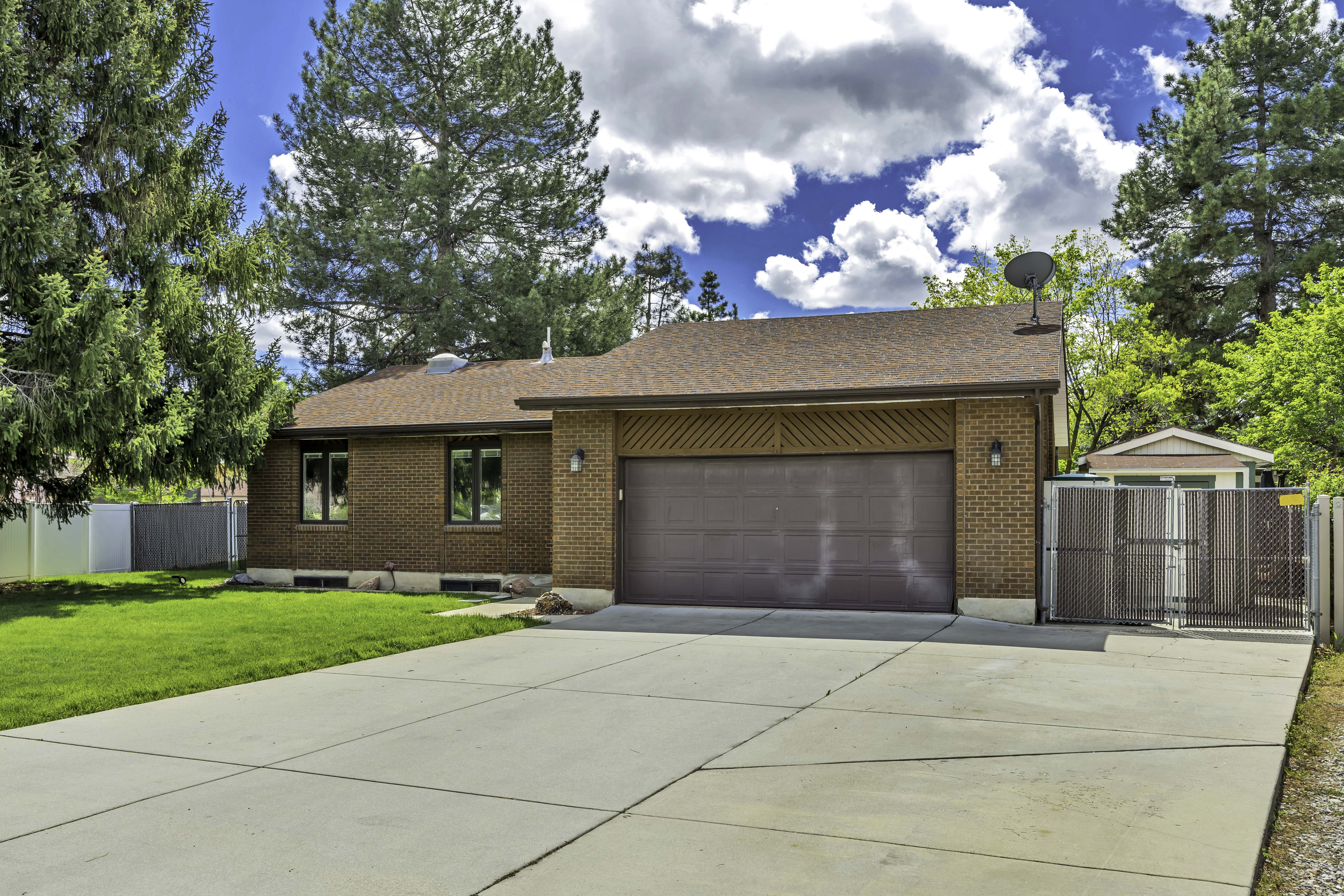 View of front of house featuring a gate, brick siding, roof with shingles, driveway, and an attached garage