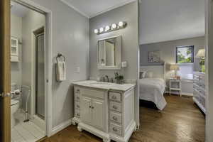 Ensuite bathroom featuring vanity, crown molding, light wood finished floors, and a stall shower