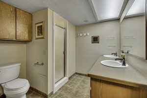 Full bathroom featuring a shower stall, light tile patterned floors, double vanity, and a textured ceiling