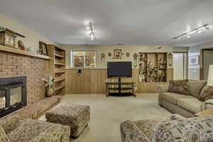 Carpeted living room with track lighting, a wainscoted wall, a brick fireplace, and wood walls