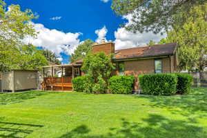 Back of property featuring brick siding, a chimney, a shed, a deck, and roof with shingles