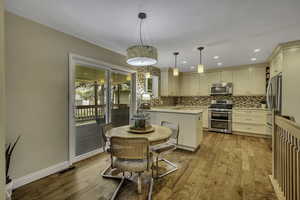Kitchen featuring cream cabinetry, stainless steel appliances, a peninsula, light wood-type flooring, and decorative backsplash