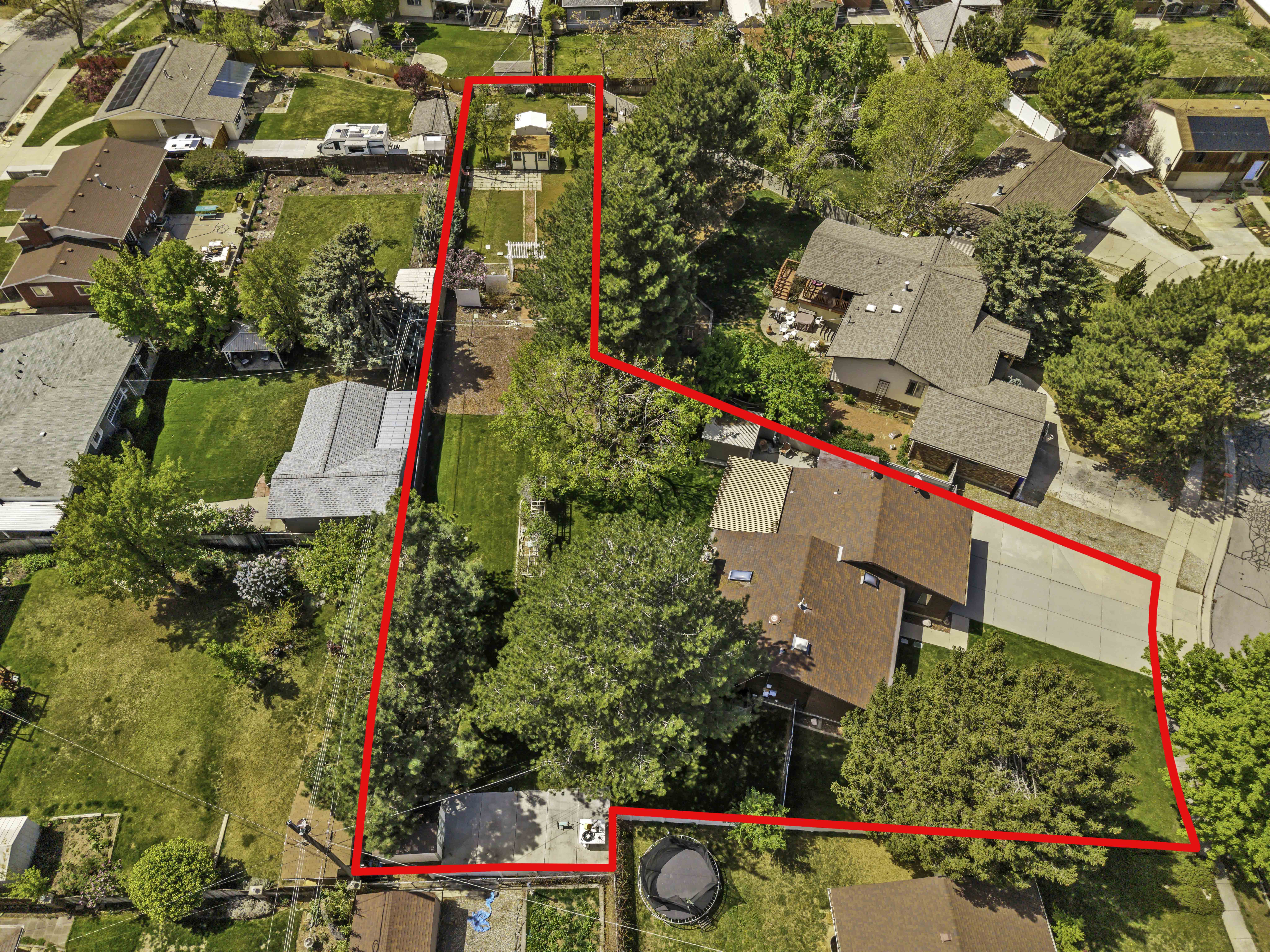 Expansive property featuring a main residence with an attached garage, a separate detached structure, mature trees, and a substantial paved driveway