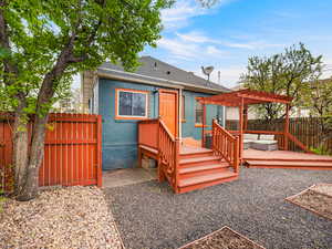 Back of house featuring a fenced backyard, roof with shingles, a deck, and brick siding