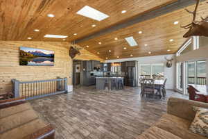 Living area featuring a skylight, recessed lighting, dark wood-style floors, wood walls, and a high wood beamed ceiling