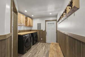 Laundry area featuring a wainscoted wall, cabinet space, light wood finished floors, wooden walls, and washer and dryer