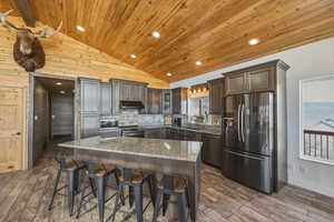 Kitchen featuring light stone countertops, stainless steel appliances, dark wood finish cabinets, a breakfast bar, and dark wood-style floors