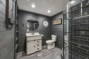Bathroom featuring wood walls, vanity, dark wood-style flooring, recessed lighting, and a tile shower