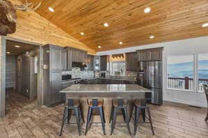 Kitchen with stainless steel appliances, light stone countertops, a breakfast bar area, dark wood-type flooring, and a vaulted wood ceiling
