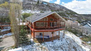 Snow covered rear of property featuring a sunroom, a deck with mountain view, a patio, and roof with shingles