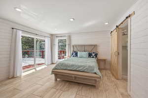 Bedroom with wood walls, a barn door, access to outside, and recessed lighting