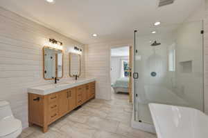Ensuite bathroom featuring double vanity, a stall shower, wood walls, a freestanding bath, and recessed lighting