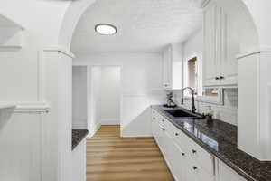 Kitchen with arched walkways, white cabinetry, a textured ceiling, light wood-style flooring, and backsplash