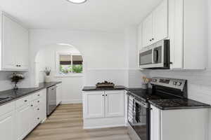 Kitchen featuring stainless steel appliances, white cabinets, dark stone counters, light wood finished floors, and decorative backsplash