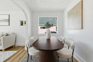 Dining space with light wood-style floors, a textured ceiling, and arched walkways