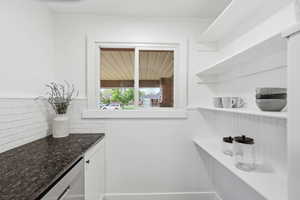 Bar area featuring dishwasher, white cabinets, a wainscoted wall, and dark stone counters