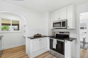 Kitchen featuring plenty of natural light, stainless steel appliances, white cabinets, light wood-style floors, and a textured ceiling