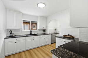 Kitchen with dark stone counters, white cabinetry, black electric stovetop, and a textured ceiling