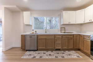 Two tone kitchen with stainless steel dishwasher, light wood finished floors, two tone cabinets, and recessed lighting