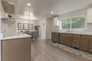Kitchen with dual tone cabinets, suspended lighting, stainless steel dishwasher, open shelves, and light wood-style floors
