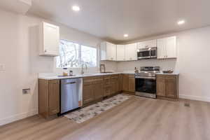 Kitchen with two tone cabinets, stainless steel appliances, light countertops, light wood-type flooring, and recessed lighting