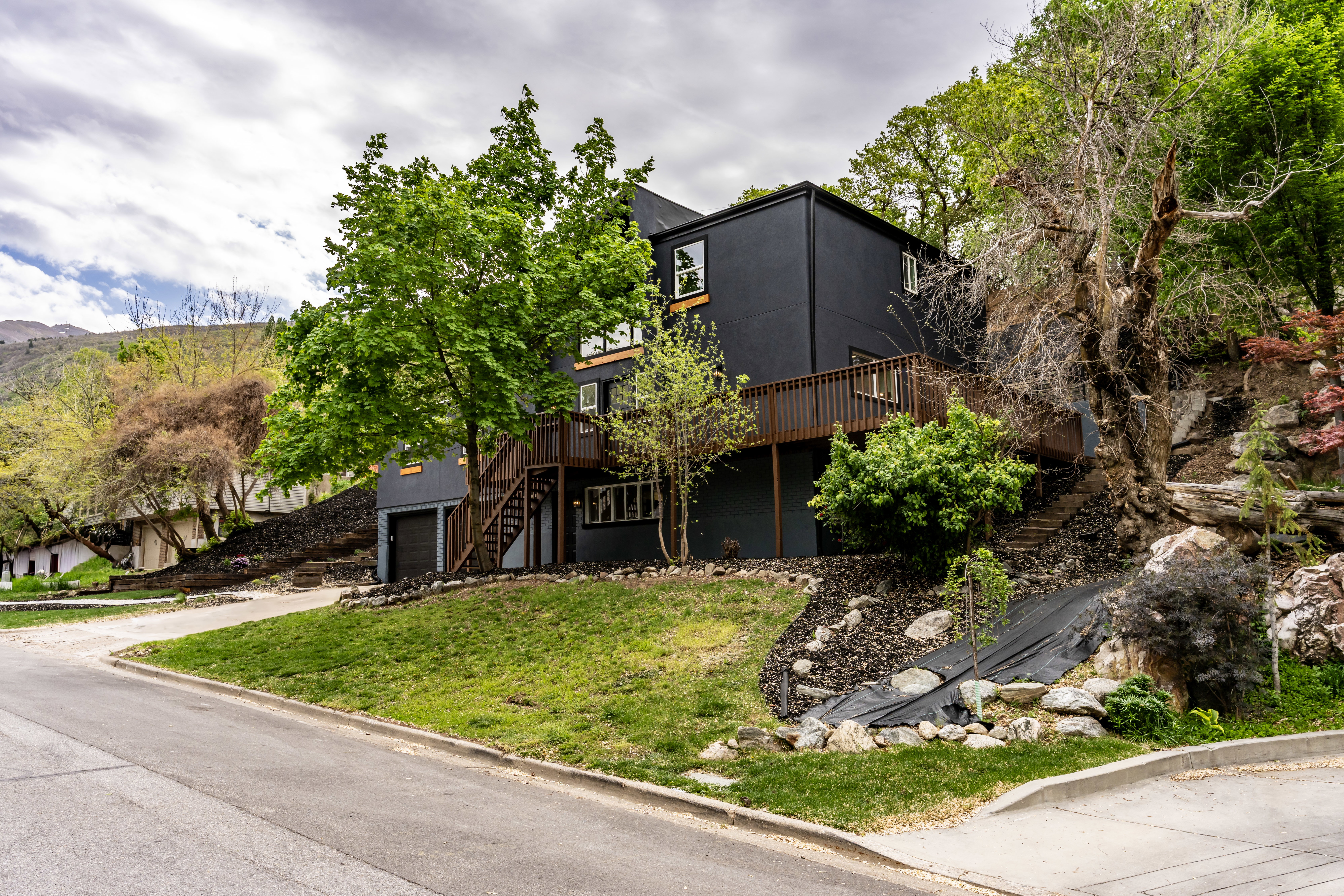 View of front facade with a deck, driveway, an attached garage, and a front lawn
