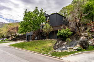 View of front facade with a deck, driveway, an attached garage, and a front lawn