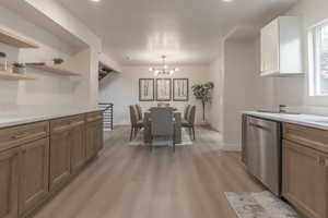 Kitchen featuring stainless steel dishwasher, a chandelier, light wood finished floors, open shelves, and light stone countertops