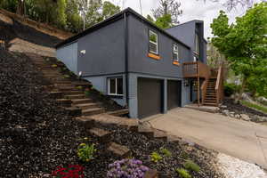 View of property exterior with stucco siding, driveway, a garage, a wooden deck, and brick siding