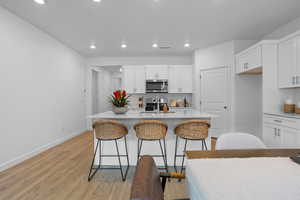 Kitchen featuring white cabinets, light stone counters, a breakfast bar area, light wood-style floors, and recessed lighting