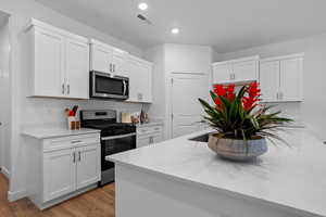 Kitchen featuring stainless steel appliances, white cabinetry, light stone counters, dark wood-style floors, and recessed lighting
