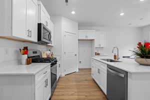 Kitchen featuring stainless steel appliances, white cabinets, an island with sink, light wood finished floors, and light stone counters
