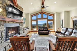 Living room with a fireplace, beam ceiling, light wood-style floors, a ceiling fan, and recessed lighting