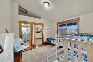 Bedroom with hardwood / wood-style flooring, lofted ceiling, and connected bathroom