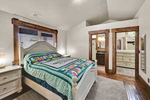 Bedroom featuring lofted ceiling, dark wood finished floors, and ensuite bath